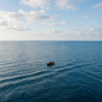 A person rowing a small wooden boat in the middle of a calm ocean under partly cloudy sky